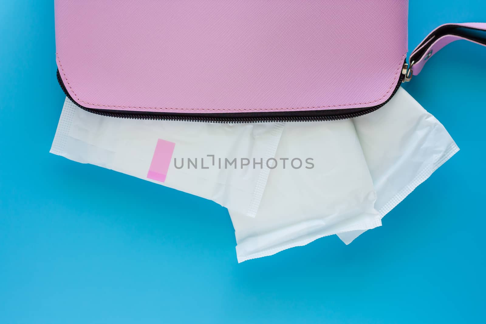 Sanitary napkin in women's pink bag on blue background for hygiene and health concept