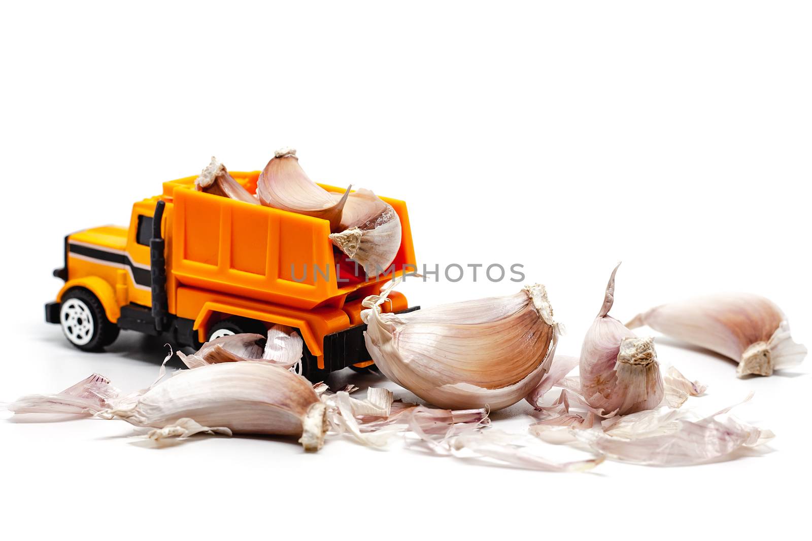 A yellow toy dump truck with garlic on white background for food and transportation concept