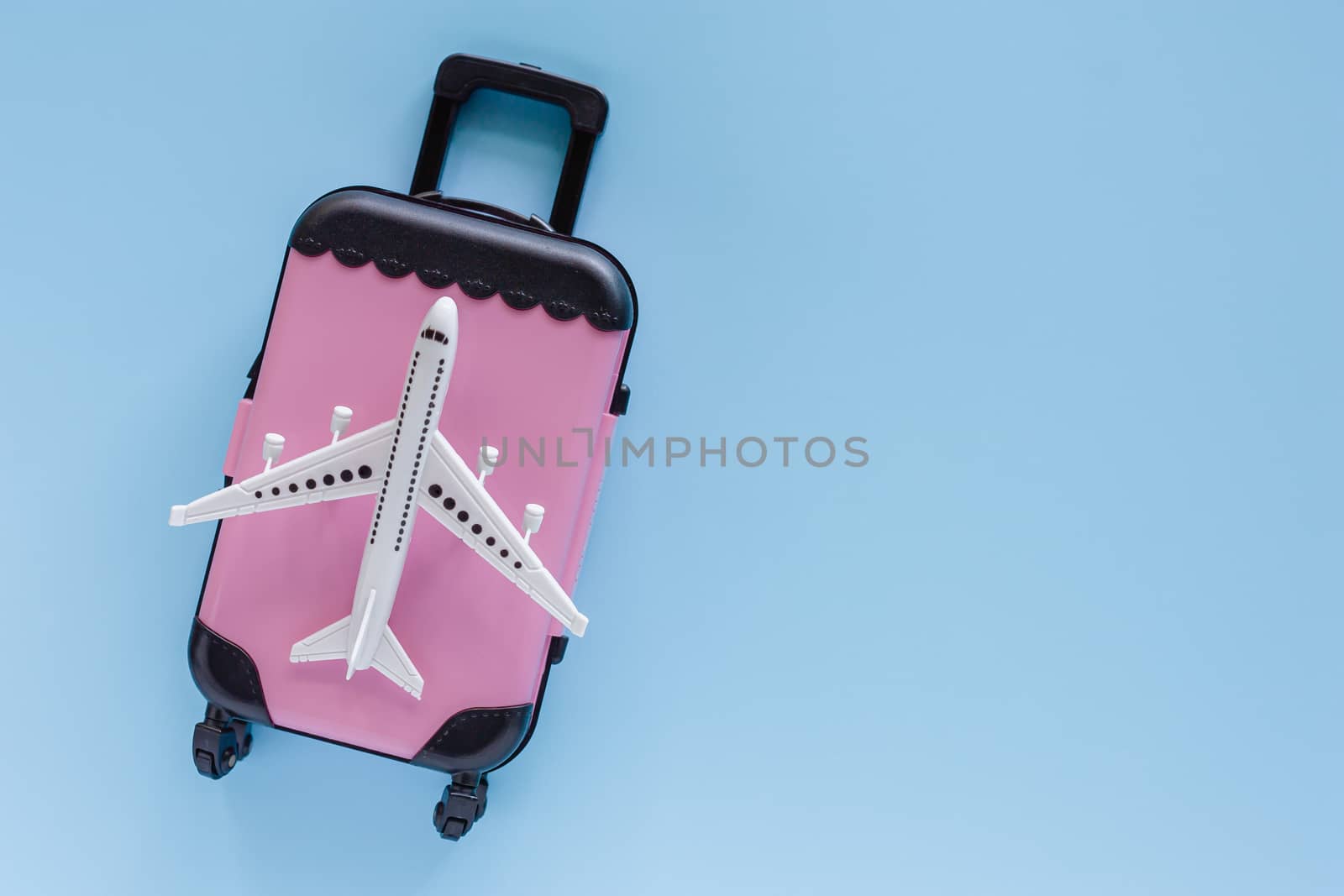 White airplane model with pink suitcase on blue background for travel and journey concept