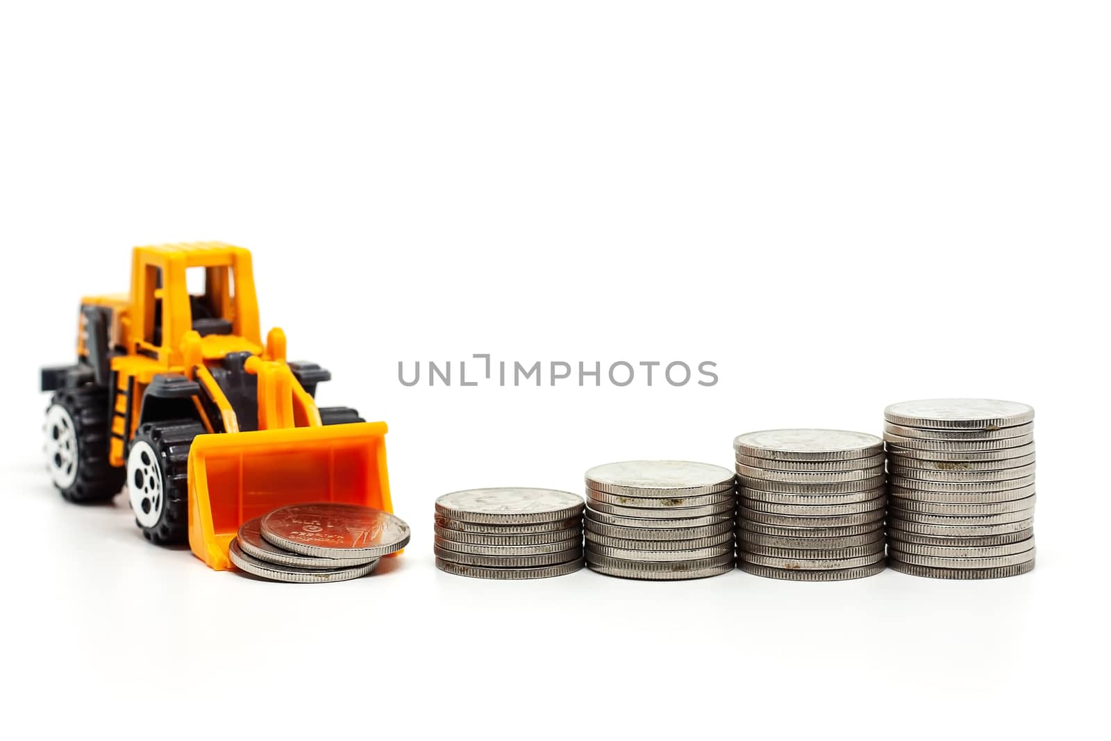 A yellow toy bulldozer with pile of coins on white background for saving money, investment, business and finance concept