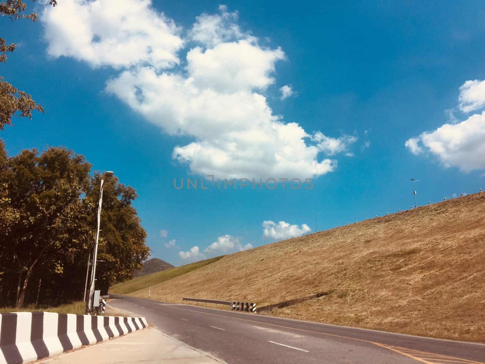 Rural country road amidst green trees with fluffy clouds and blue sky background for travelling and transportation concept