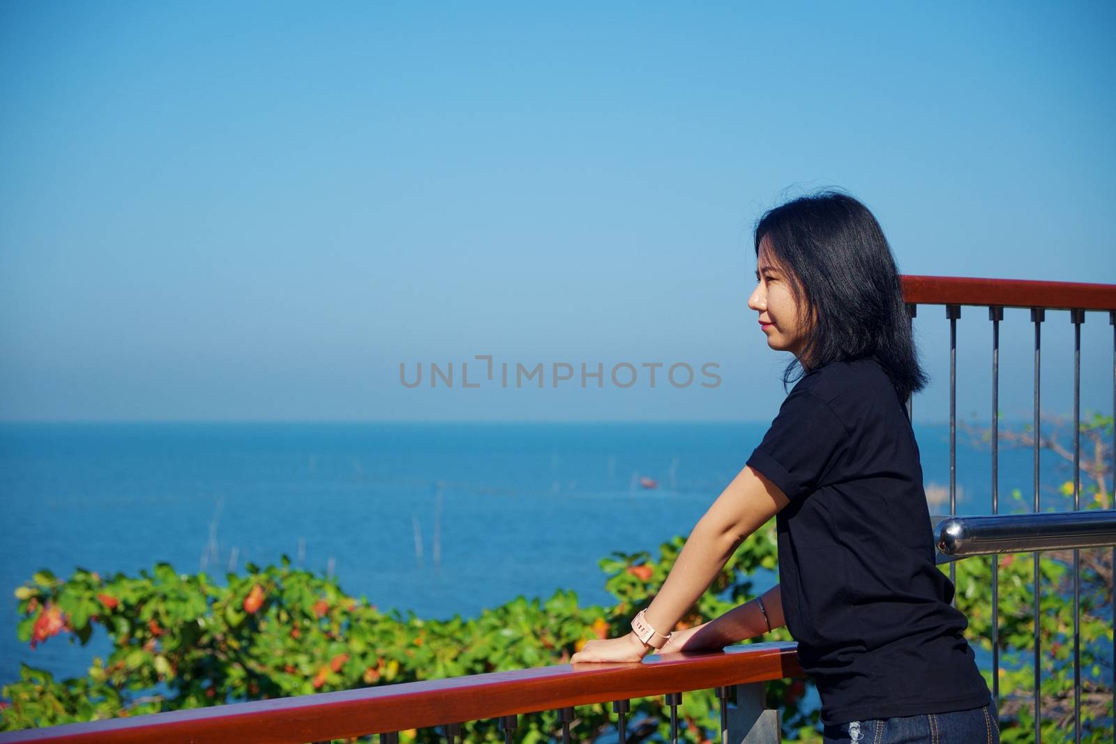 Young asian woman in black shirt standing and looking forward at sea viewpoint with blue sky background