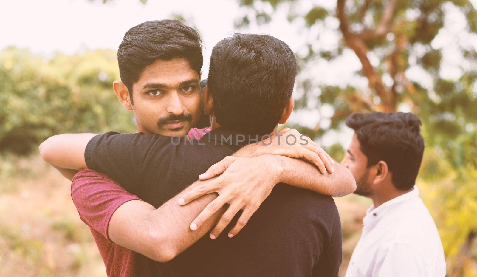 Concept of fake hug, friendship, embracing - Young Hypocritical boy embracing a friend at outdoors - Friend hugging and looking at camera.