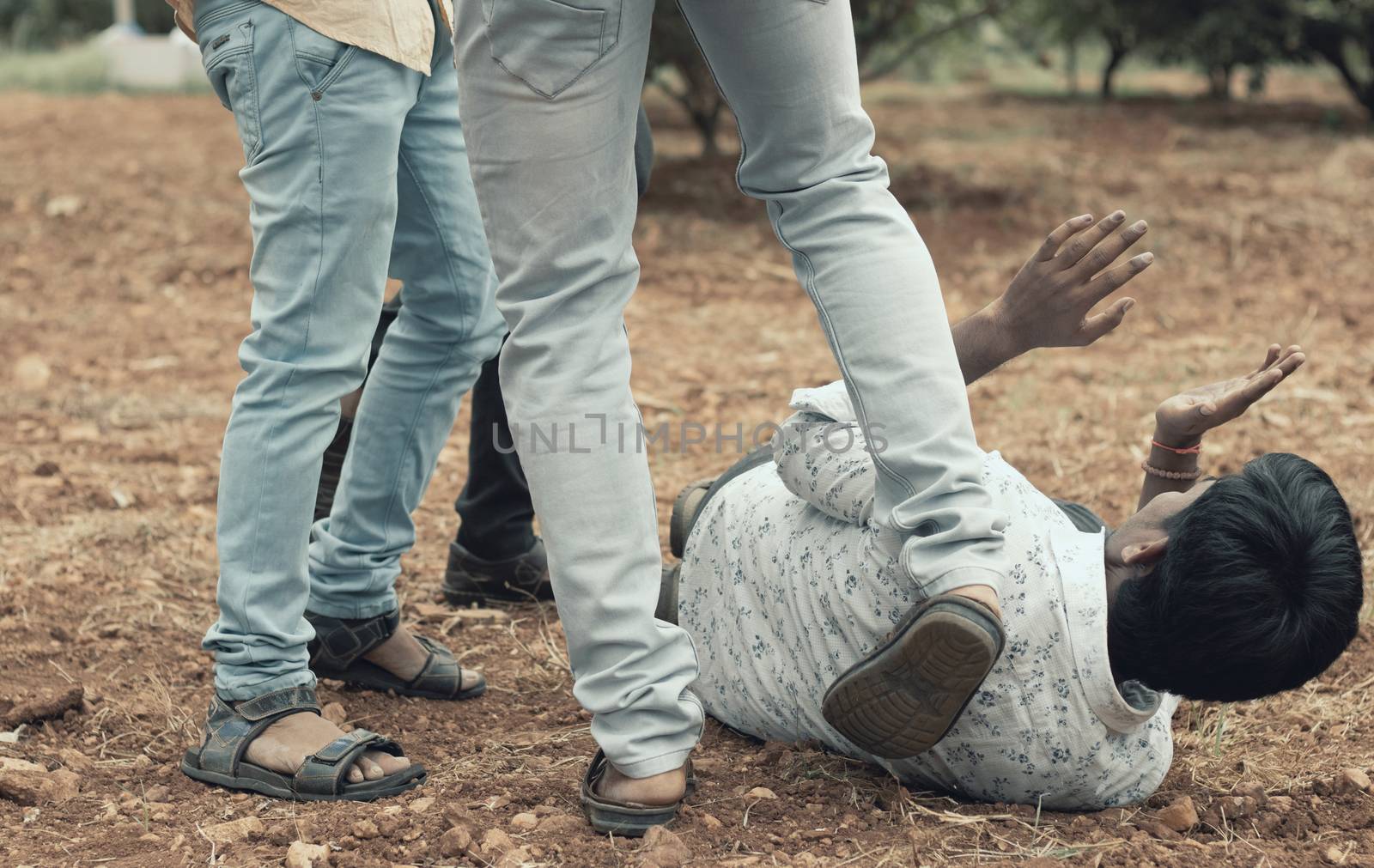 Concept of mob lynching - Group of people bullying, kicking a man - Close up of young adult males hitting a person on ground.