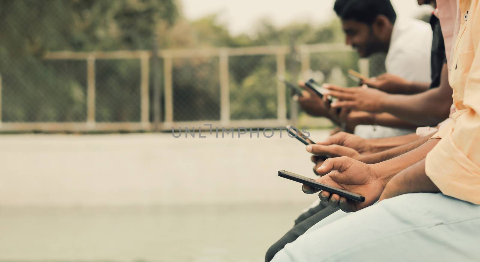 Close up of hands,young people being addicted to devices - friends group sitting in queue using phones at swimming pool - Concept of Millennials busy on smartphones and technology with copy space. by lakshmiprasad.maski@gmai.com