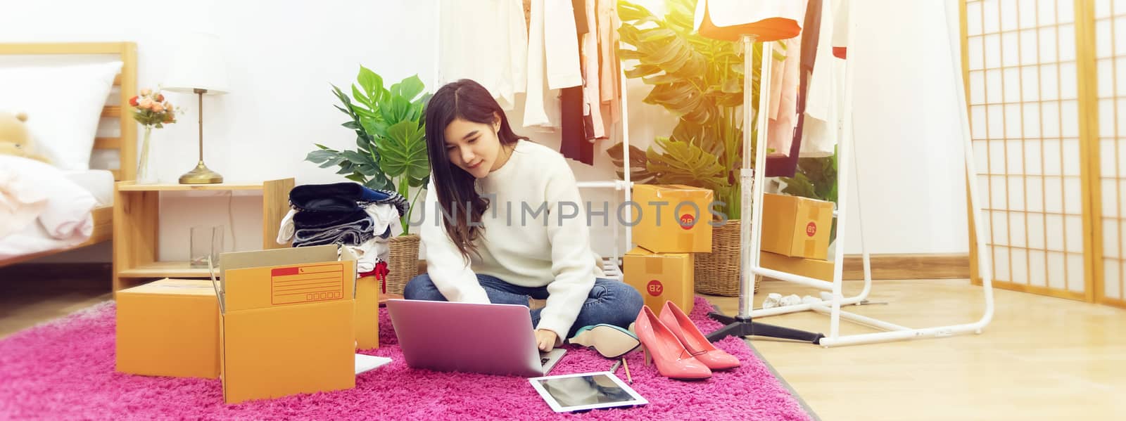 work from home. happy female selling products online, start up small business owner using laptop computer on wooden floor with fashion clothes accessories and postal parcel in her room