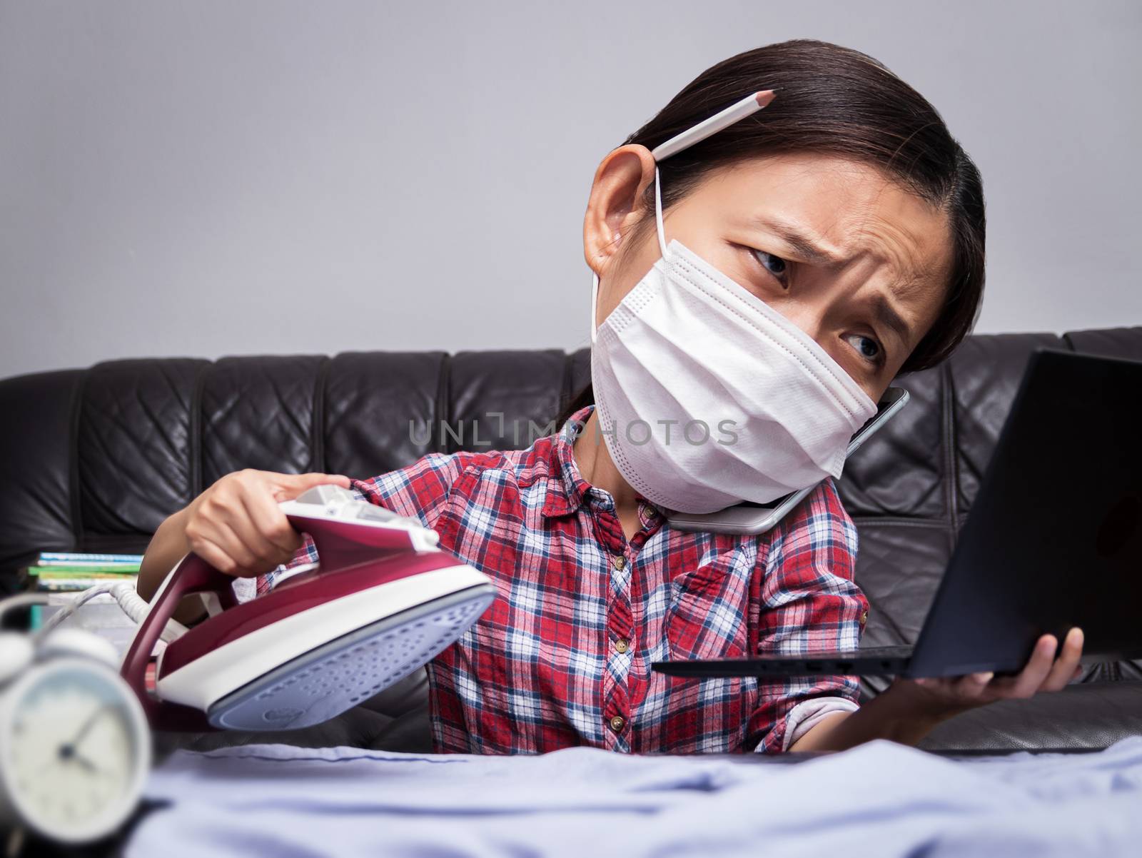 woman working with very busy business and housework part, ironing cloth, talking on phone and working with laptop during self isolation to avoid spreading illness transmission of COVID-19 Coronavirus