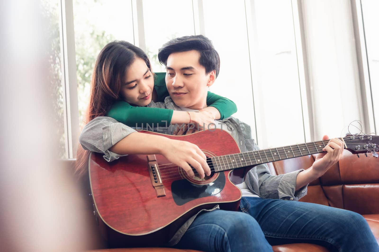 Young Couple Love Having Fun While Sing a Song and Playing Guitar in Living Room Together, Portrait of Couple are Relaxing at Their Home. Romantic Lifestyles an Valentine's Day Concept