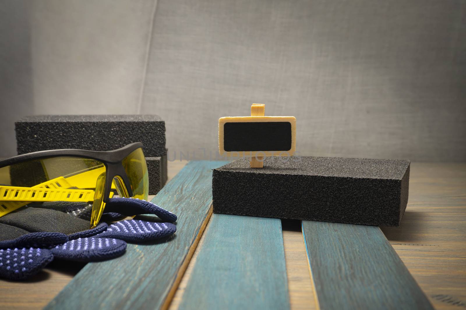 DIY renovation concept with safety gloves and goggles, abrasive sponges and plank of upright wood in close up