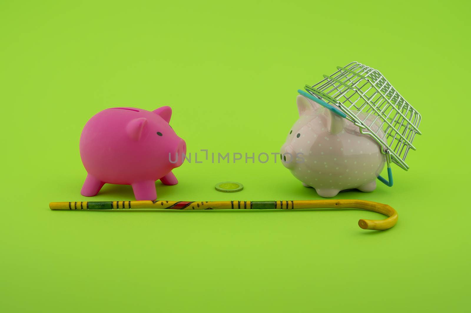 Saving for old-age and retirement concept with two piggy banks, shopping basket, coin and walking stick over a green background with copy space