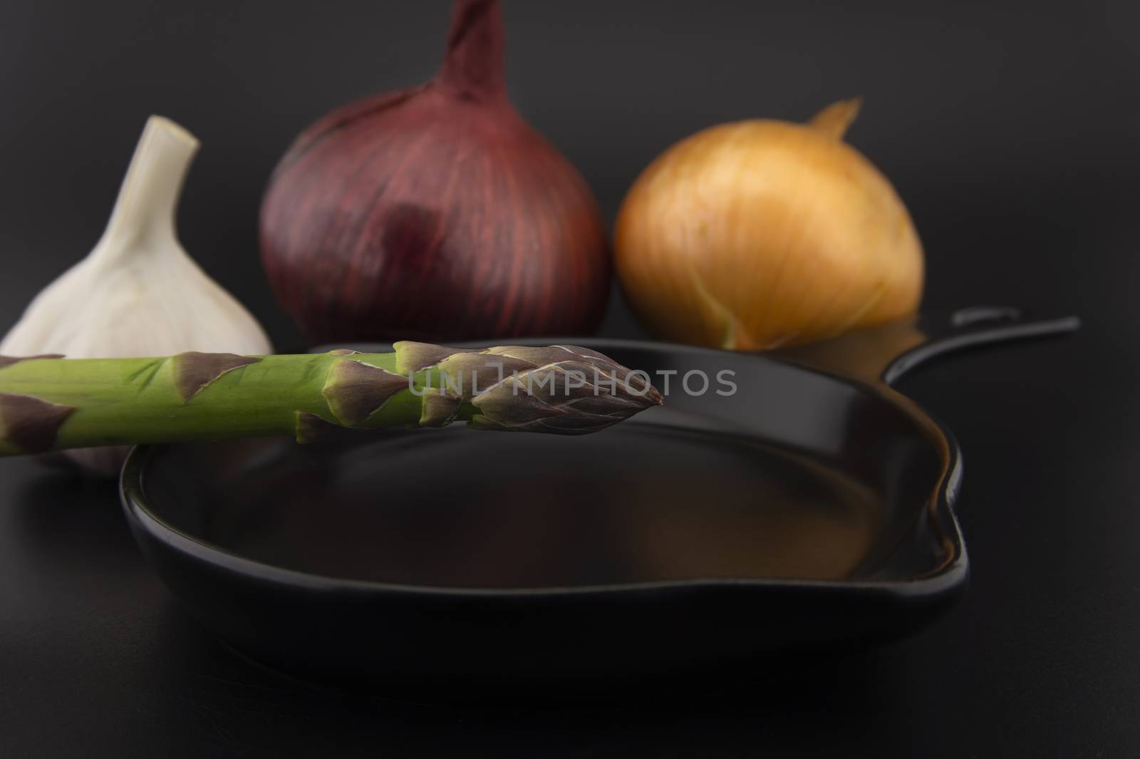 Skillet with fresh raw green spring asparagus spears and assorted red and white onions with garlic bulb ready for cooking