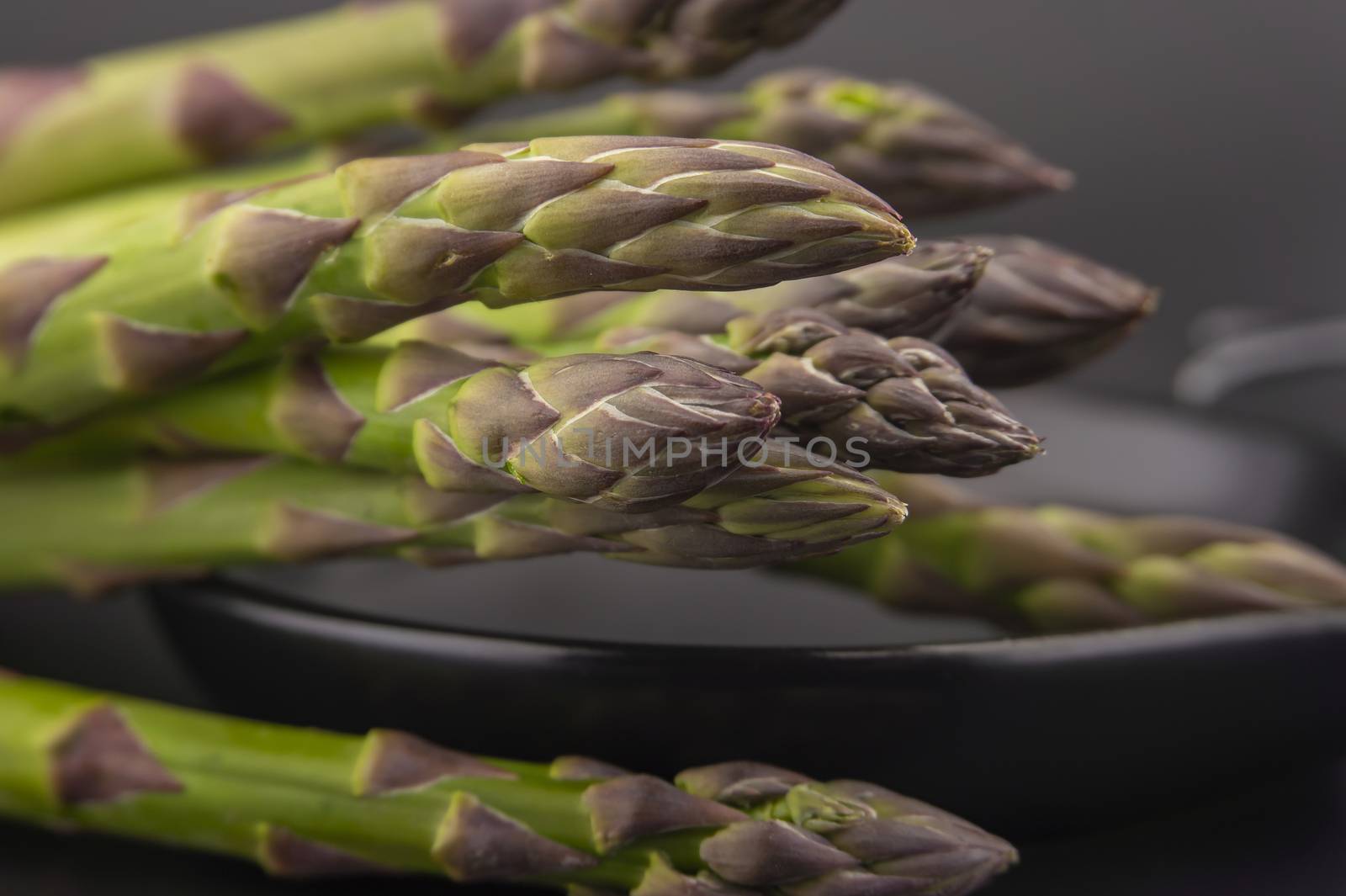 Skillet with fresh raw green spring asparagus spears ready for cooking over a black background with copy space