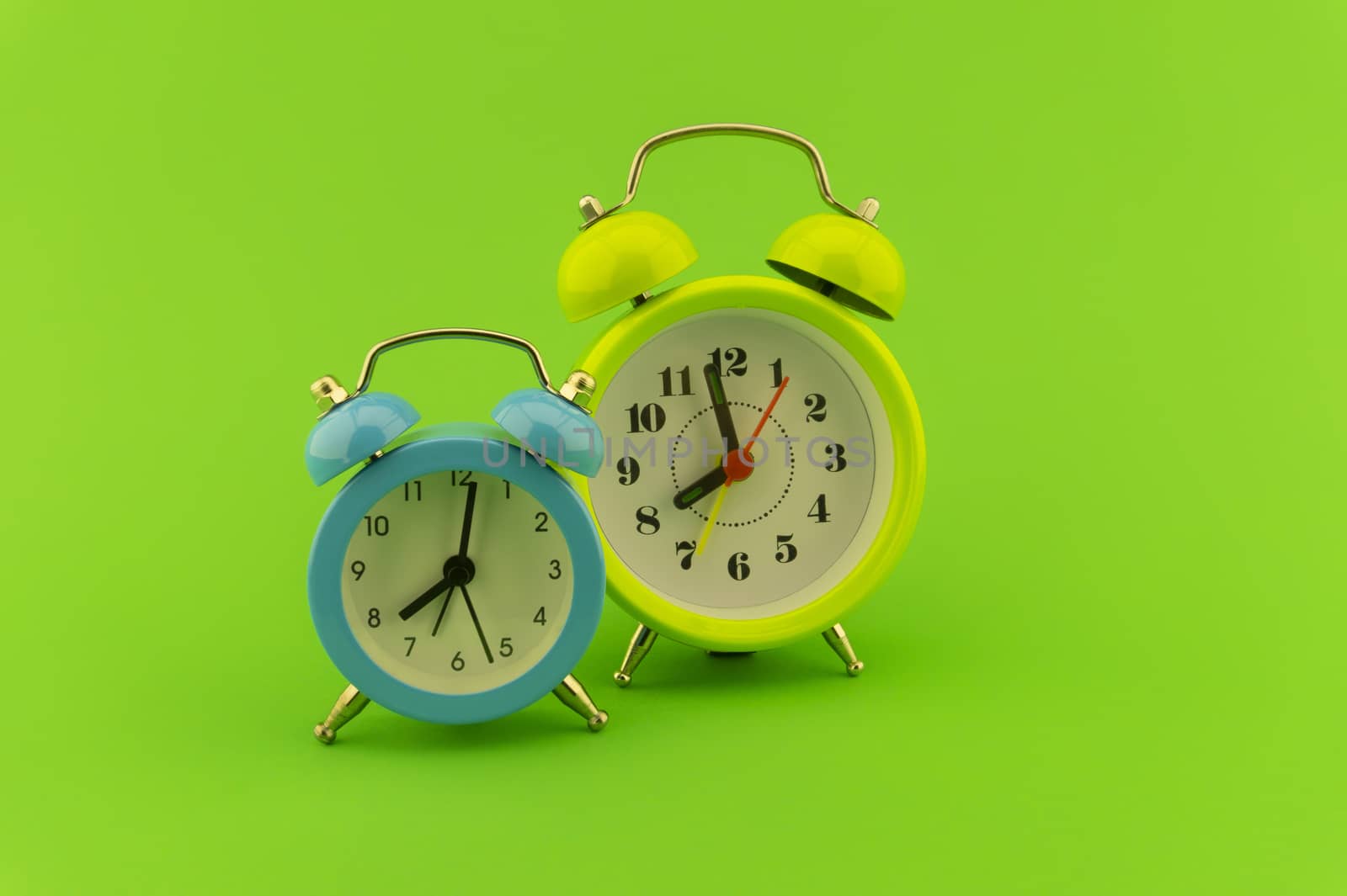 Blue and yellow twin bell analog alarm clocks over a colorful green background with copy space