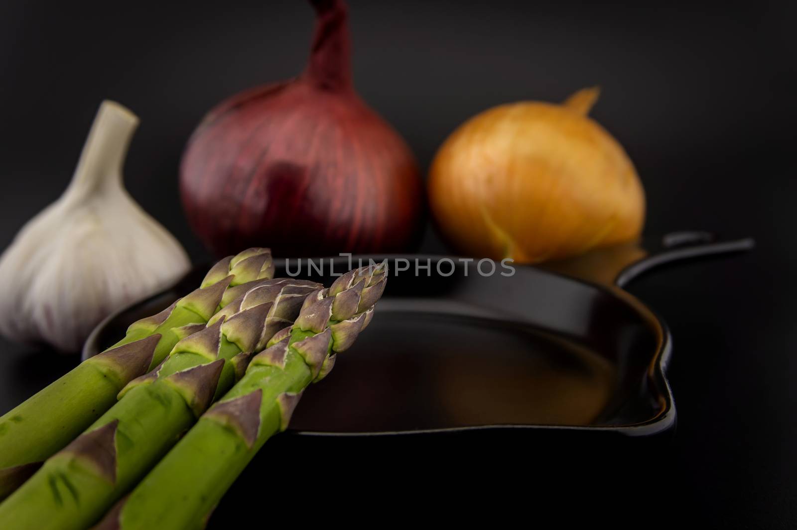 Skillet with fresh raw green spring asparagus spears and assorted red and white onions with garlic bulb ready for cooking