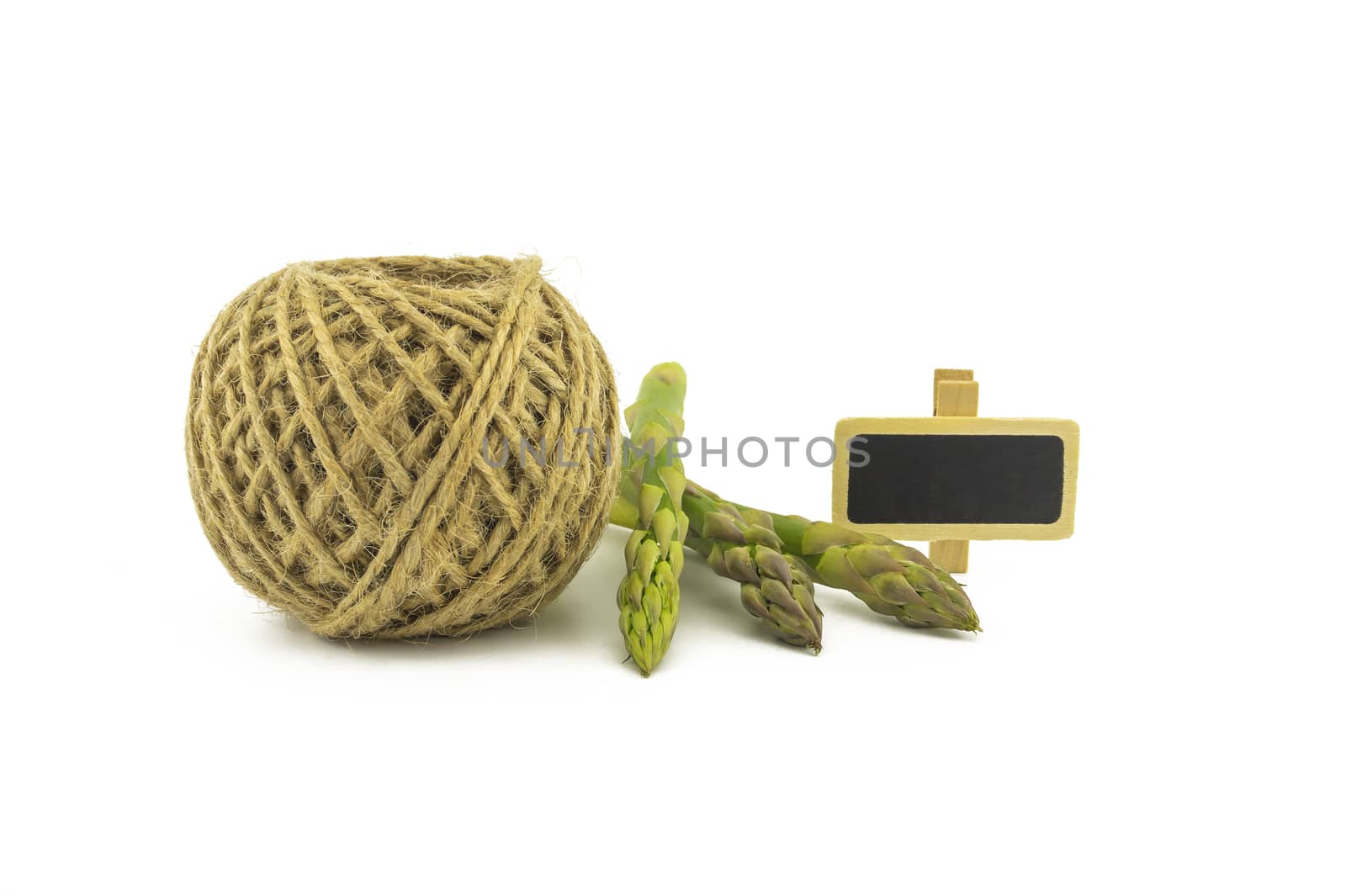 Fresh green asparagus spears and ball of natural hemp twine alongside a small slate or signboard isolated on white background, selective focus in a low angle view