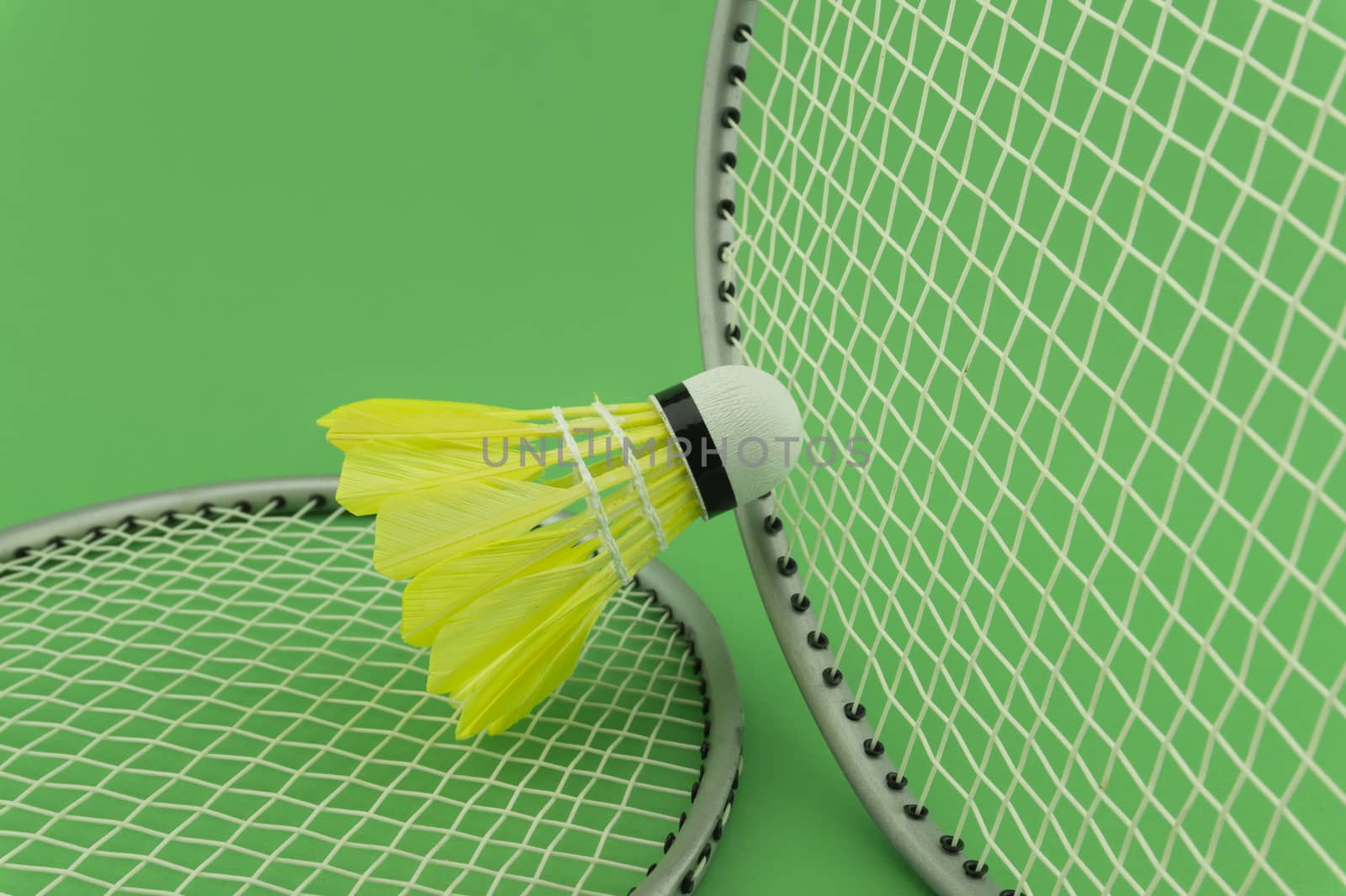 Badminton rackets and yellow feathered shuttlecocks on green background in a close up view