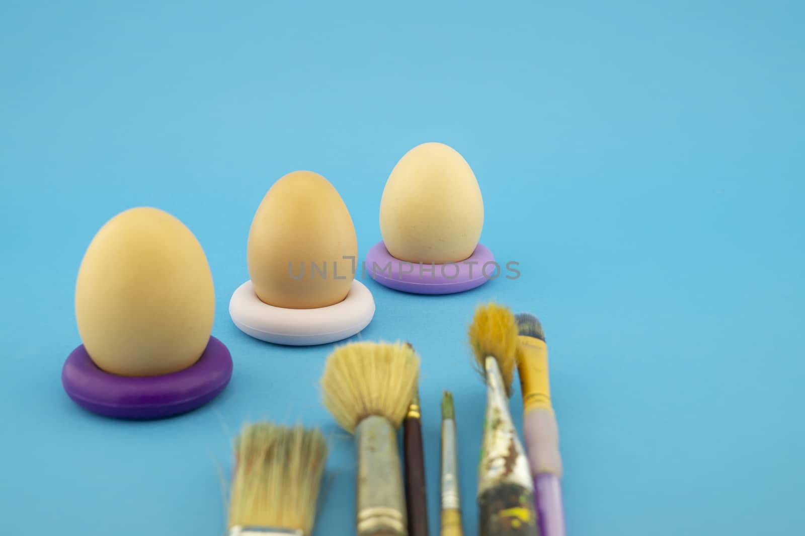 Easter eggs coloring concept with three unpainted eggs and set of different paint brushes, on blue background