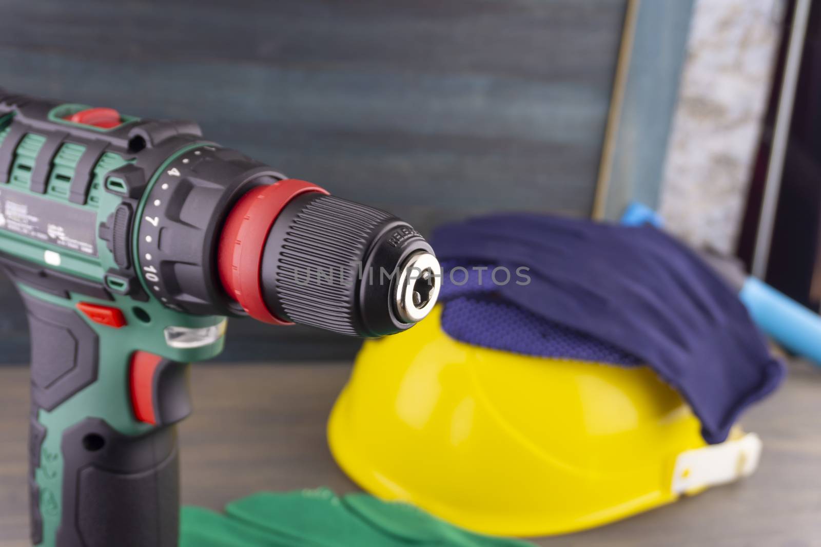 Electric drill and yellow protective helmet and pairs of new blue gloves on a workbench, blurred in background. Construction tools and work equipment in close-up with copy space