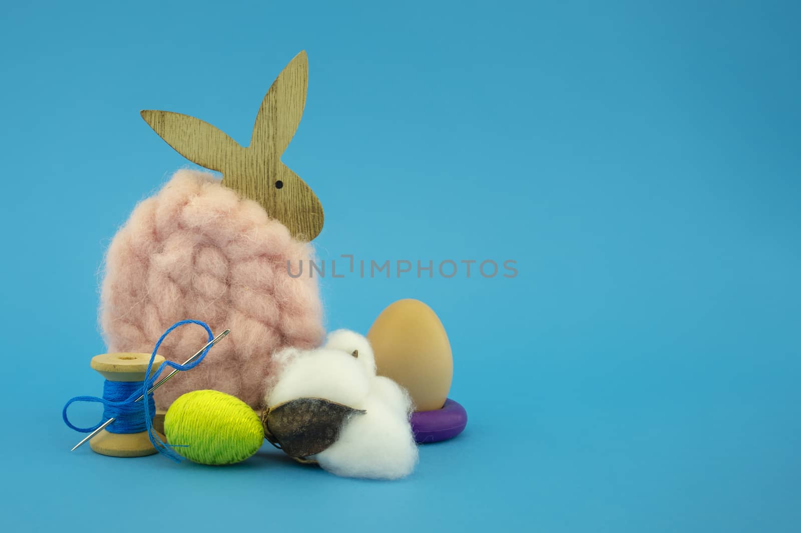 Colorful creative Easter still life with handicrafts featuring egg on purple ring, a natural fluffy cotton or wool rabbit over blue