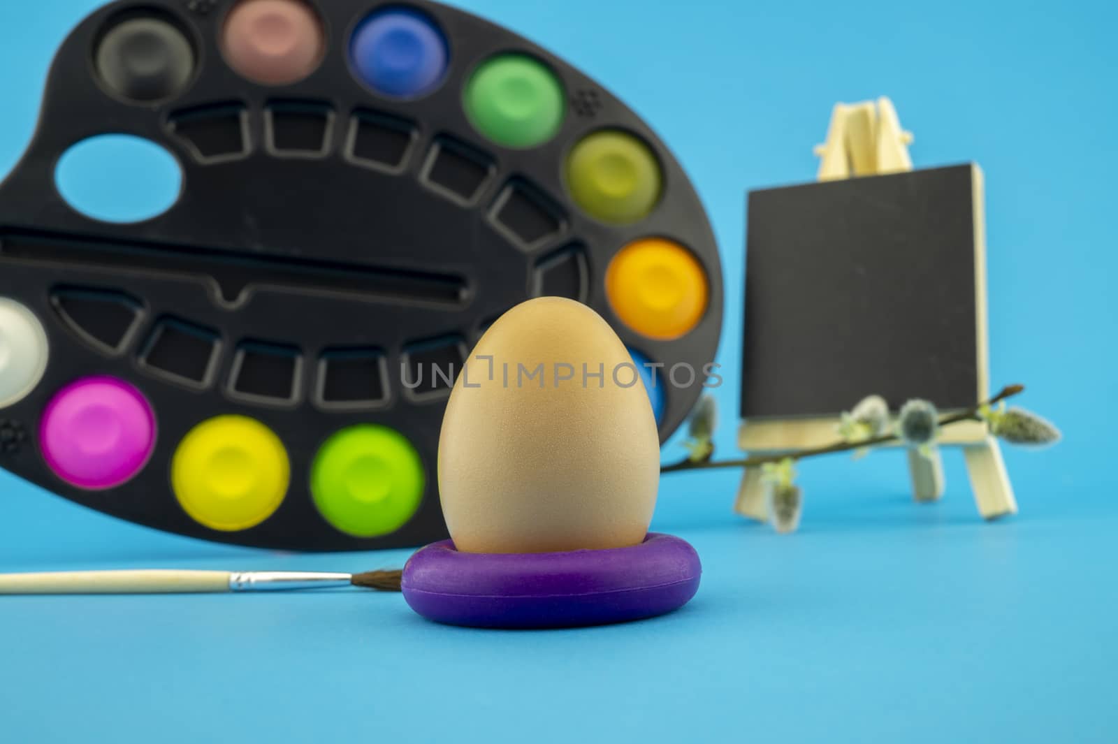 Easter egg decoration concept with paint brushes and set of watercolor paints in pallet. Studio still life on blue background