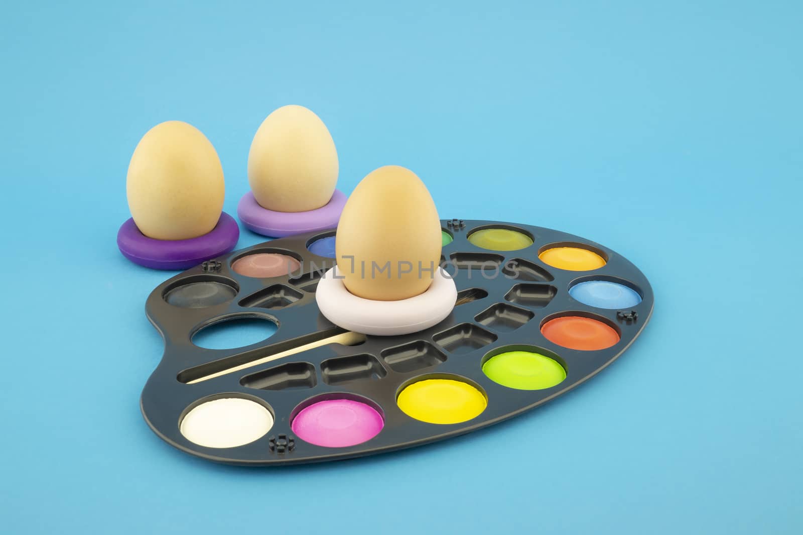 Easter egg decoration concept with blank blackboard and set of watercolor paints in pallet. Studio still life on blue background