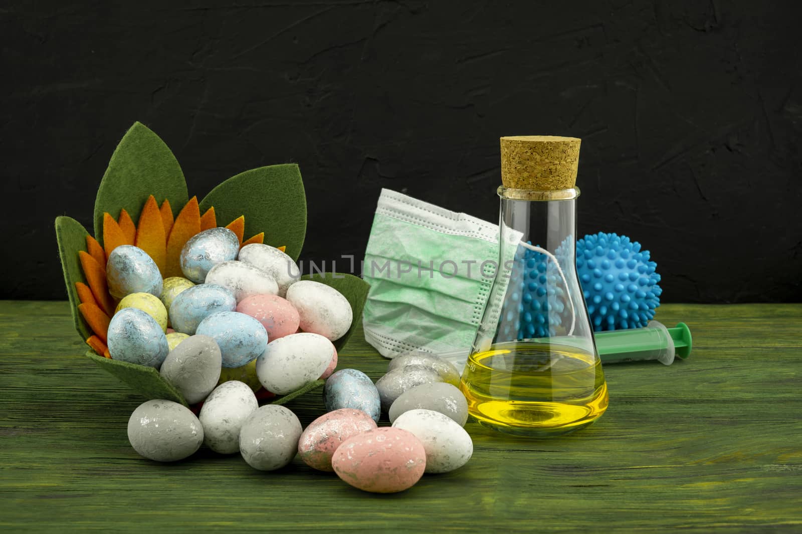 Virus pandemic and celebrating Easter concept with syringe and a protection mask, two blue virus molecules and glass container next to a Easter arrangement with traditional painted eggs