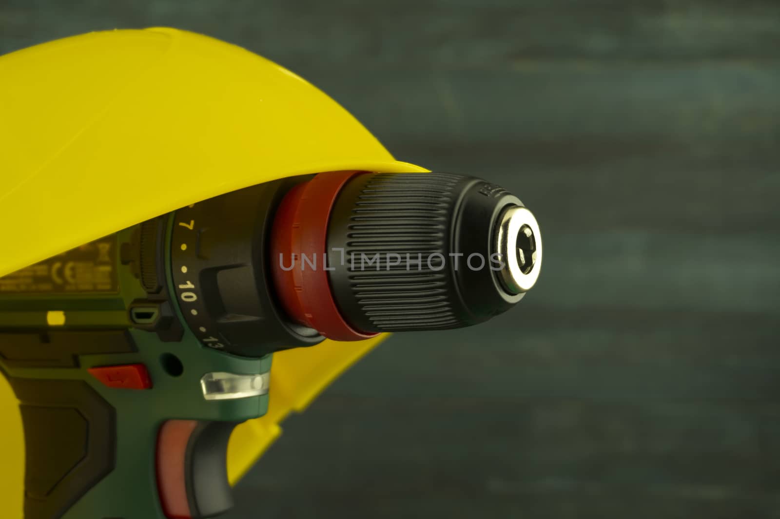 Cordless drill under yellow hardhat on a workbench, blurred in background. Construction tools and work equipment in close-up with copy space