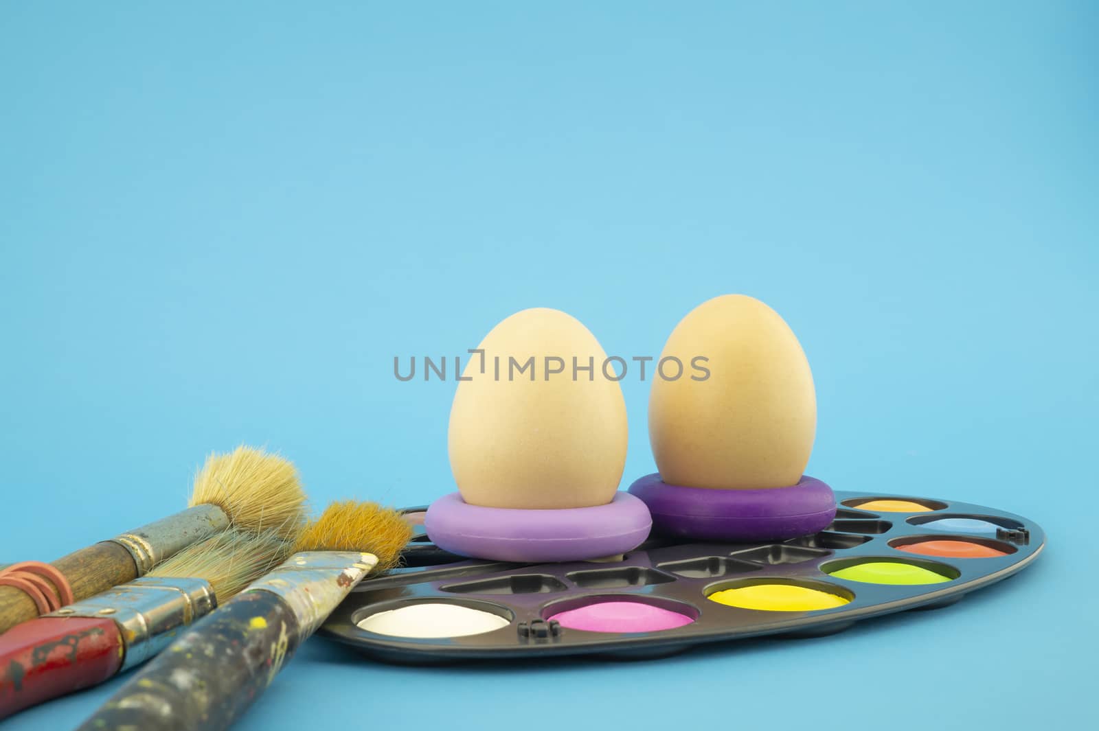 Easter eggs coloring concept with three unpainted eggs and set of different paint brushes, on blue background