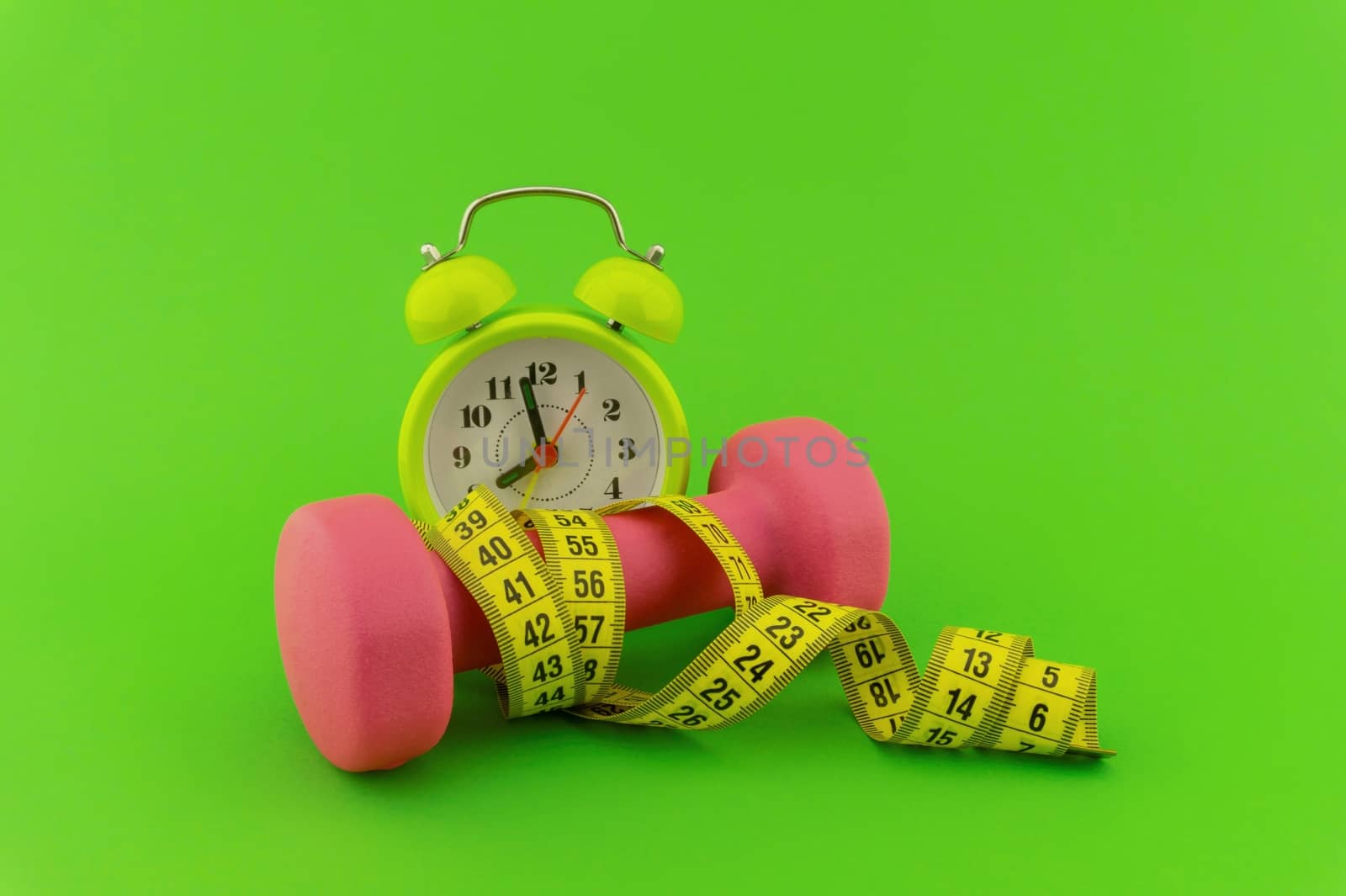 Starting healthy lifestyle concept. Still life with pink dumbbell, measuring tape and alarm clock on green background