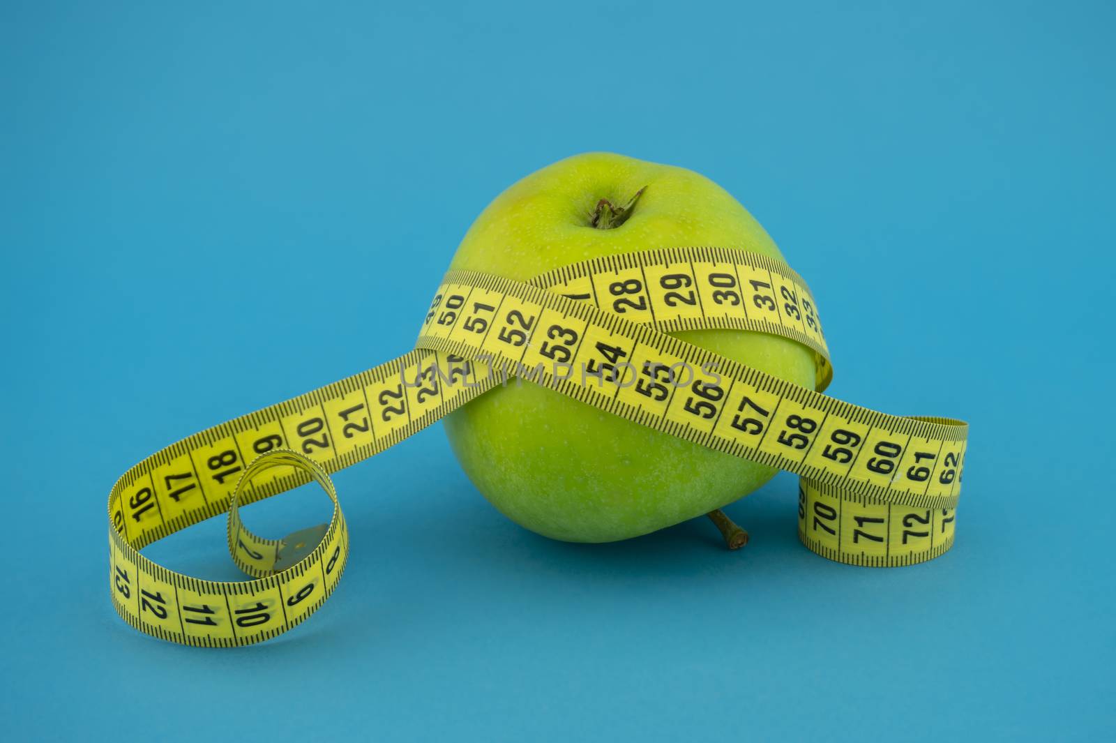 Weight loss and healthy diet concept with measuring tape and green apple on blue background