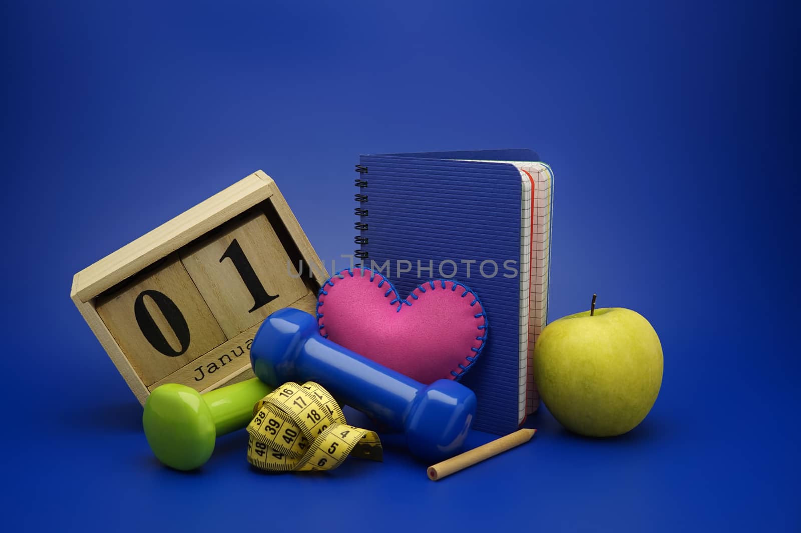 Starting healthy lifestyle on the first day of the year concept. Still life with dumbbells, measuring tape, calendar and new notebook on blue background