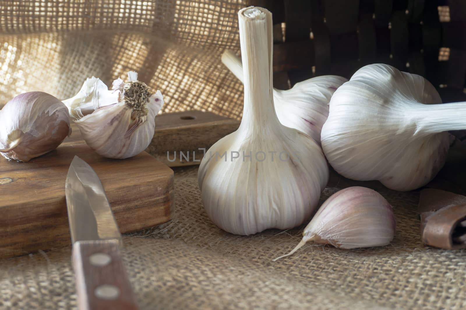 Garlic bulbs in close-up on sack cloth with kitchen knife and wooden cutting board