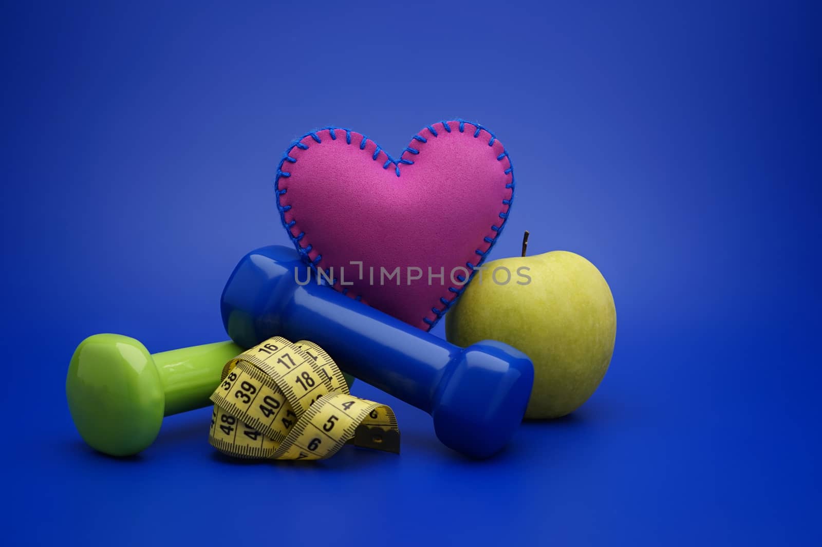 Still life with small dumbbells, measuring tape and green apple, as a concept of healthy nutrition and sports diet in close-up on blue background