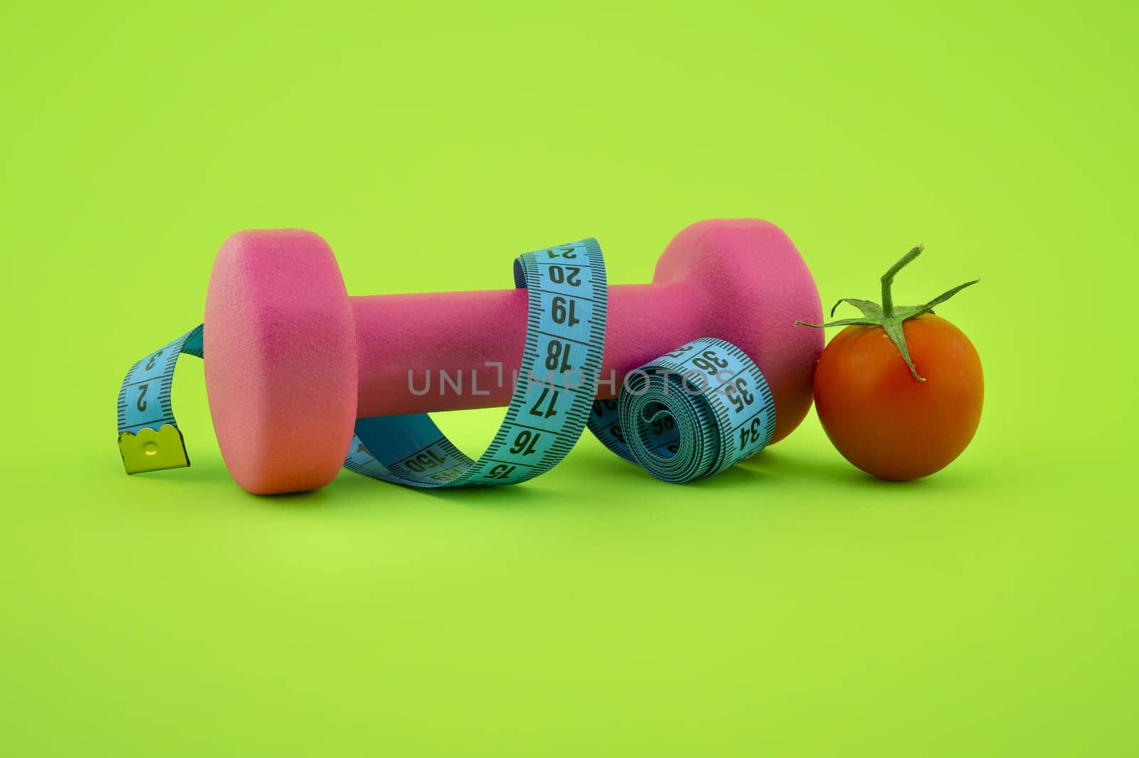 Still life with small dumbbells, measuring tape and cherry tomato, as a concept of healthy nutrition and sports diet in close-up on green background