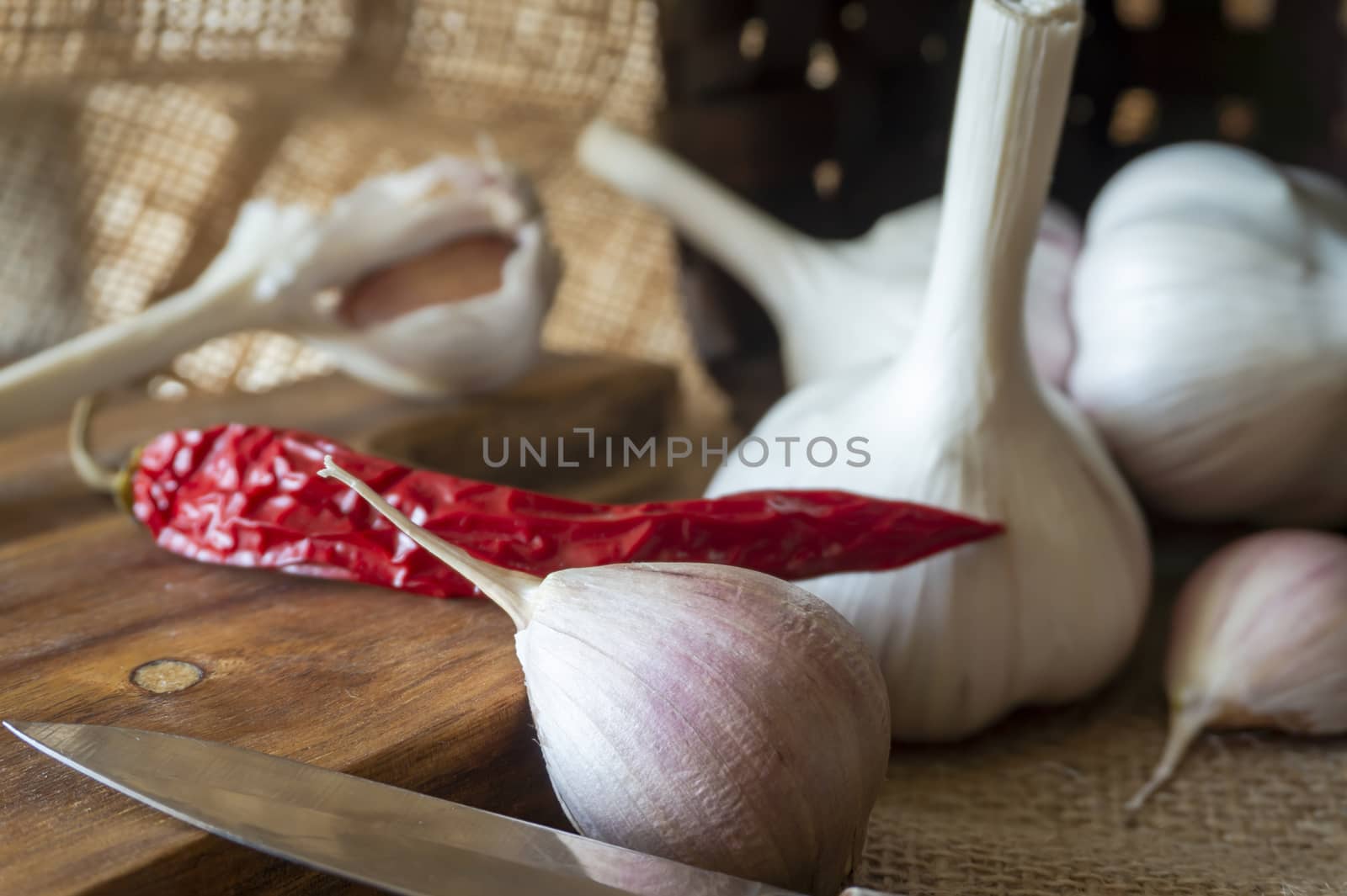 Garlic cloves, bulbs and red chilli pepper in close-up on sack cloth with kitchen knife and wooden cutting board