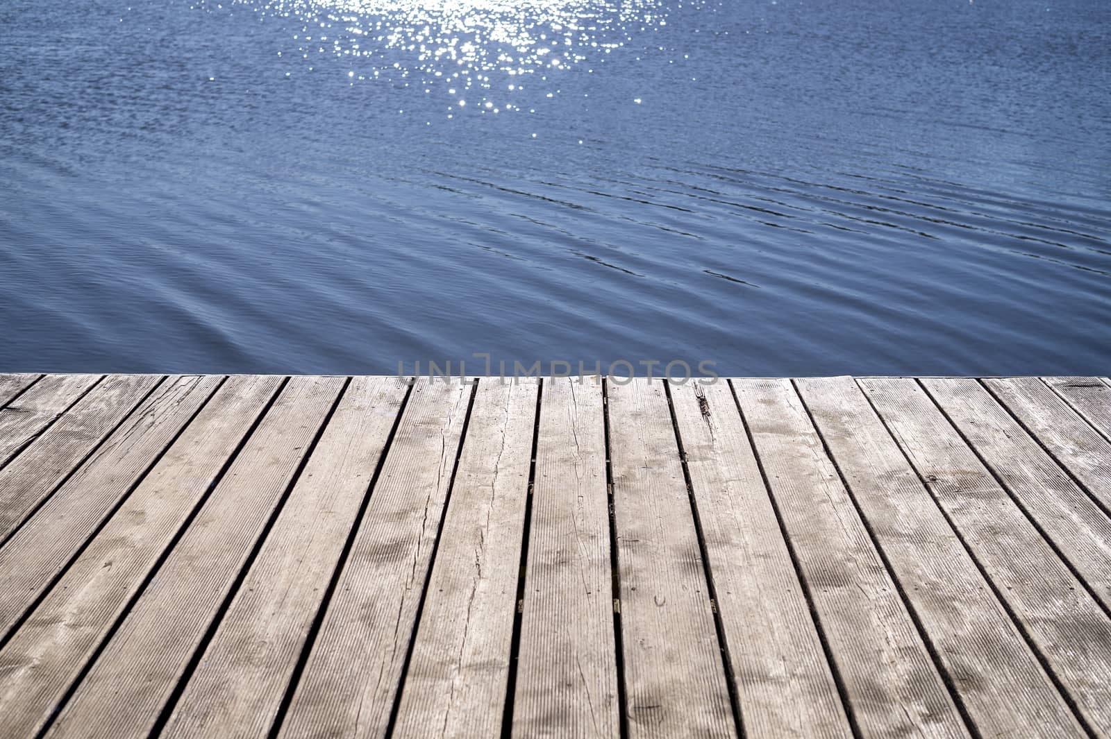 Wooden textured boards of a jetty and reflection of the sun on the water in a low angle view