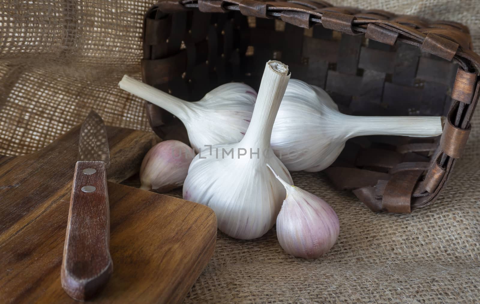 Garlic bulbs and cloves in close-up on sack cloth with kitchen knife and wooden cutting board