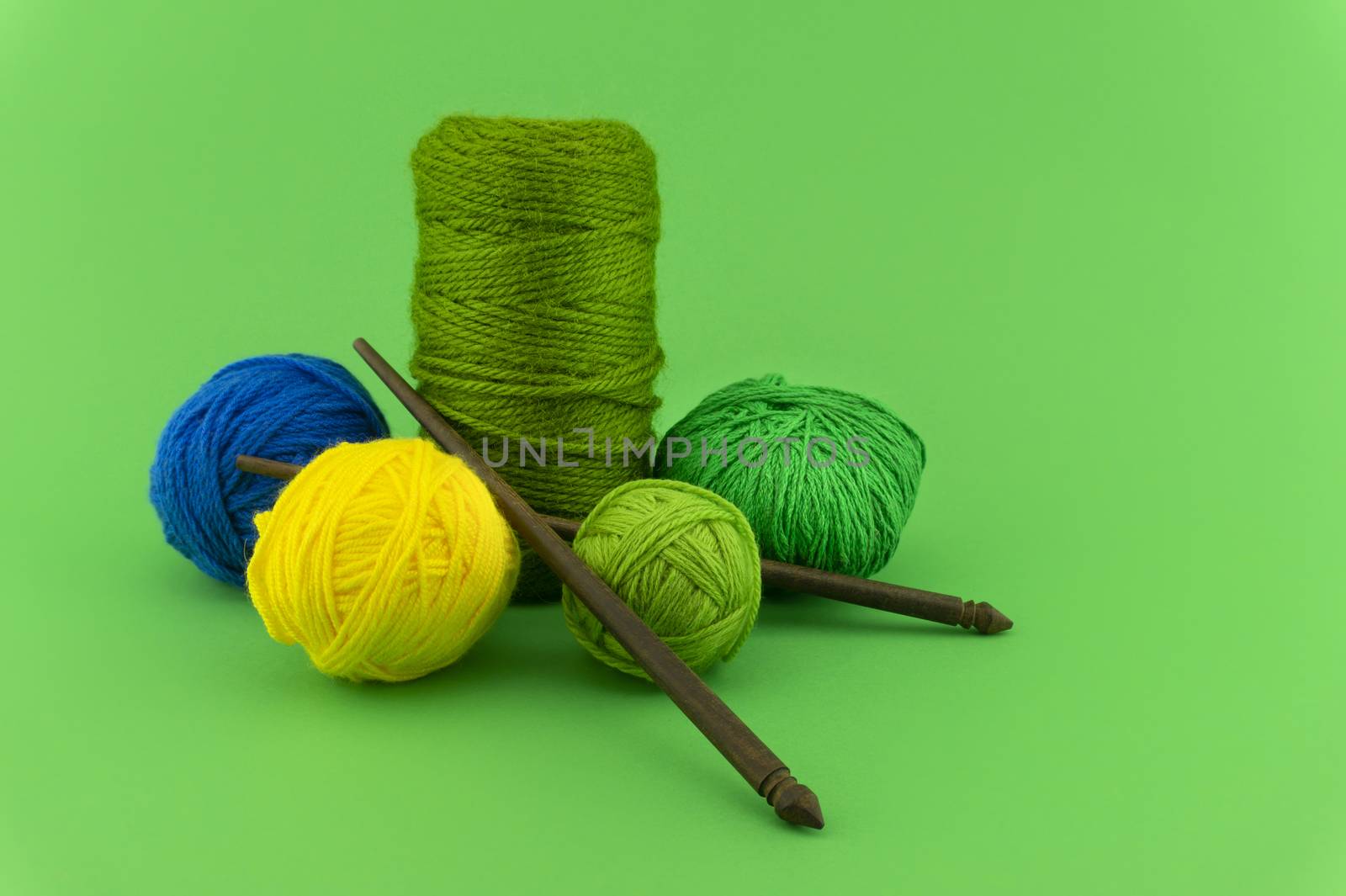 Green, blue and yellow knitting yarn or wool on colorful green background with knitting needles