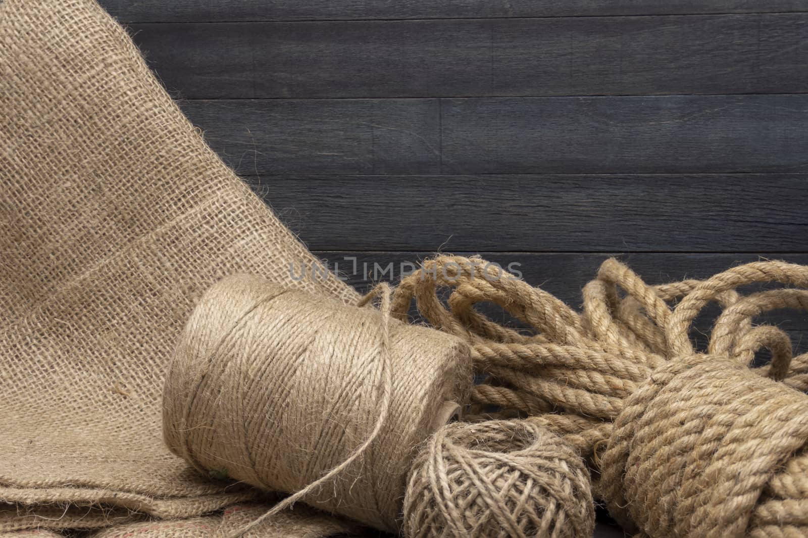 Two spools of burlap threads or jute twine and coil of linen rope on sackcloth fabric in close-up on grey background