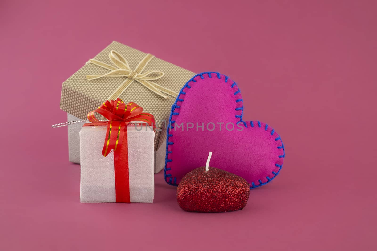 Romantic still life with hand sewn textile pink heart, candle, decorative gifts and red envelope on pink background with copy space