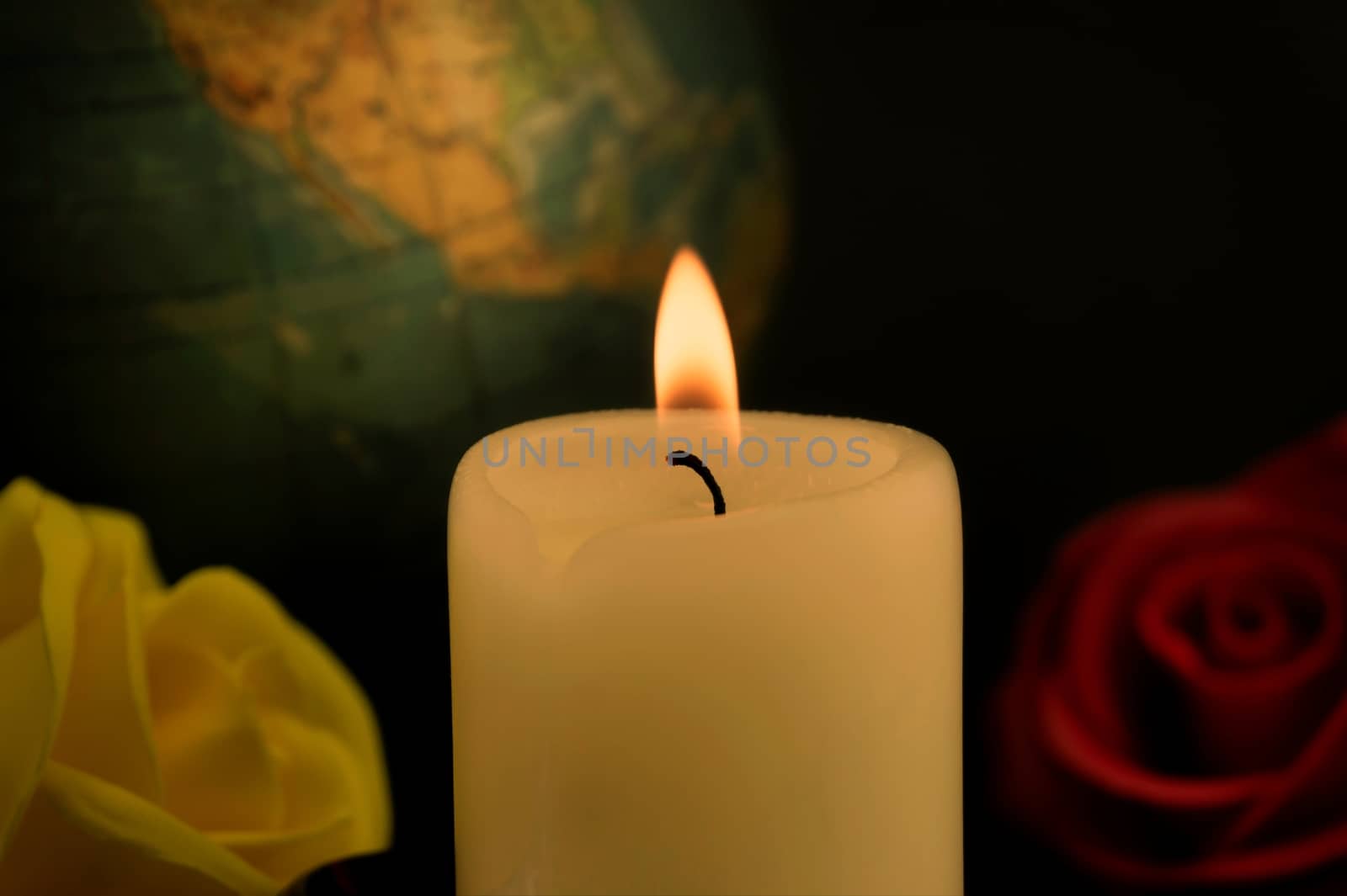 Single burning yellow candle in front of a globe next to red and yellow roses against dark background, concept of global disasters and deaths