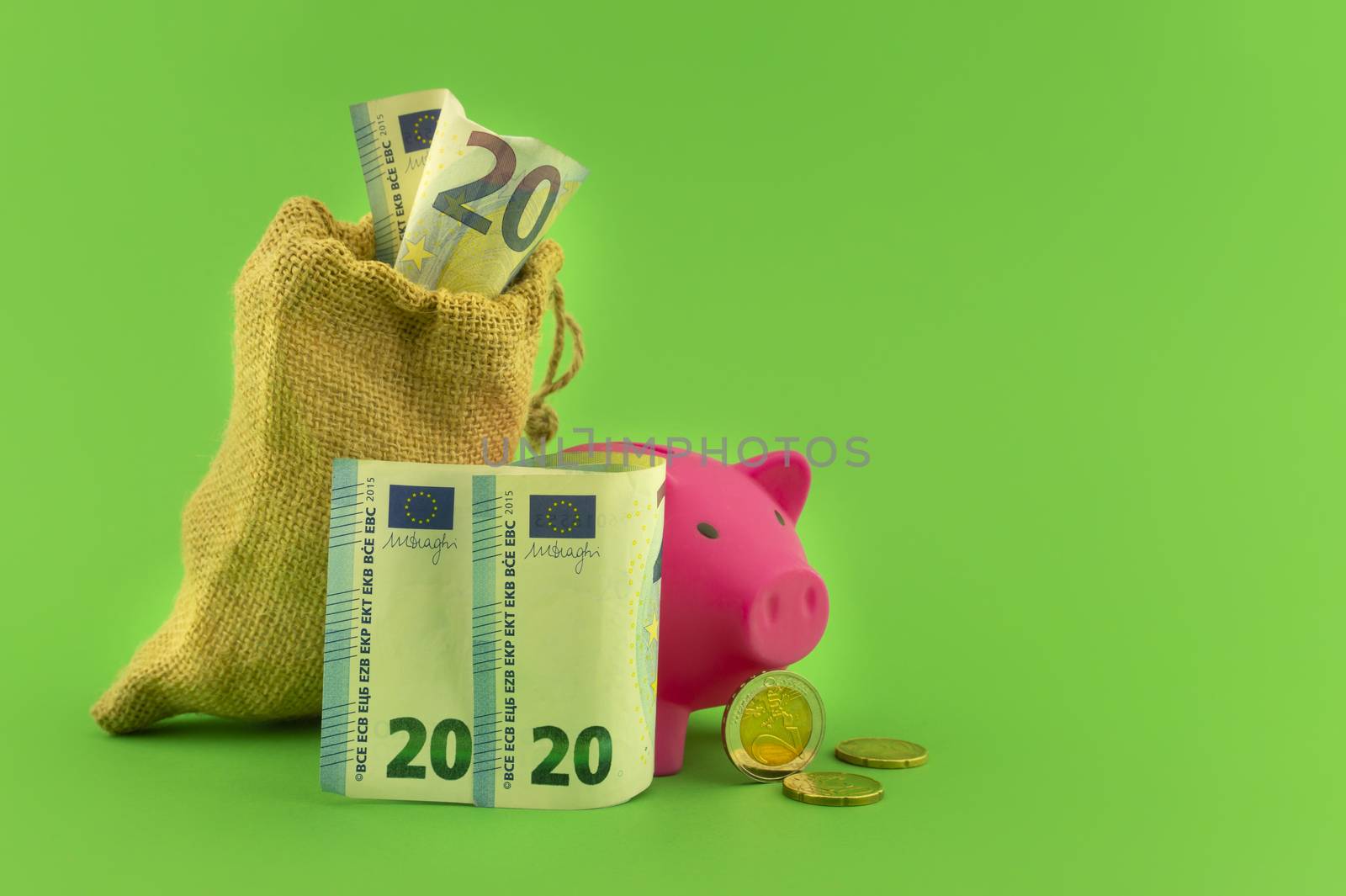 Reaping the rewards of financial success with a cute pink piggy bank, sack of money with a twenty Euro bill in the slot over a green background