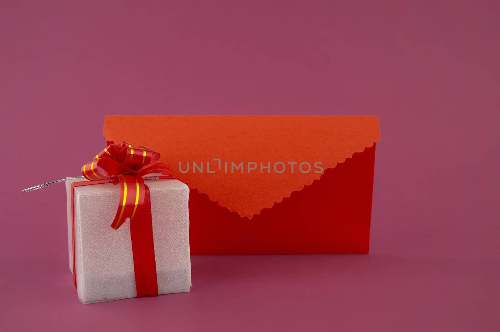 Romantic still life with decorative gift and red envelope on pink background with copy space