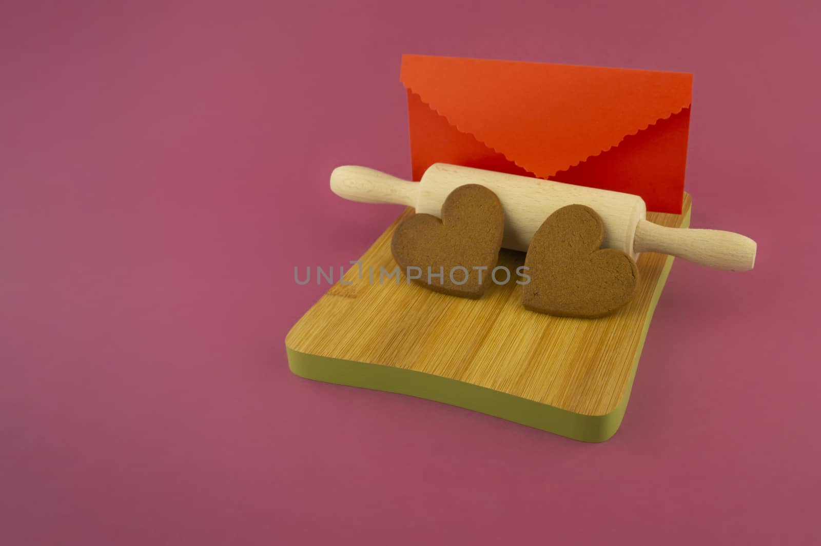 Message with love concept with two heart shaped cookies and red envelope on pink background with copy space