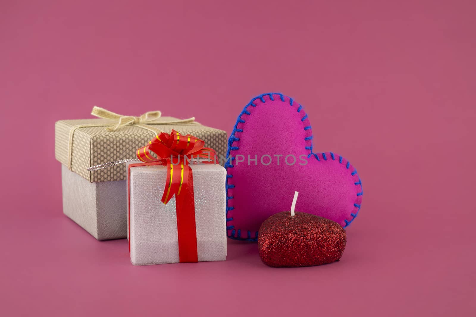 Romantic still life with hand sewn textile pink heart, candle, decorative gifts and red envelope on pink background with copy space
