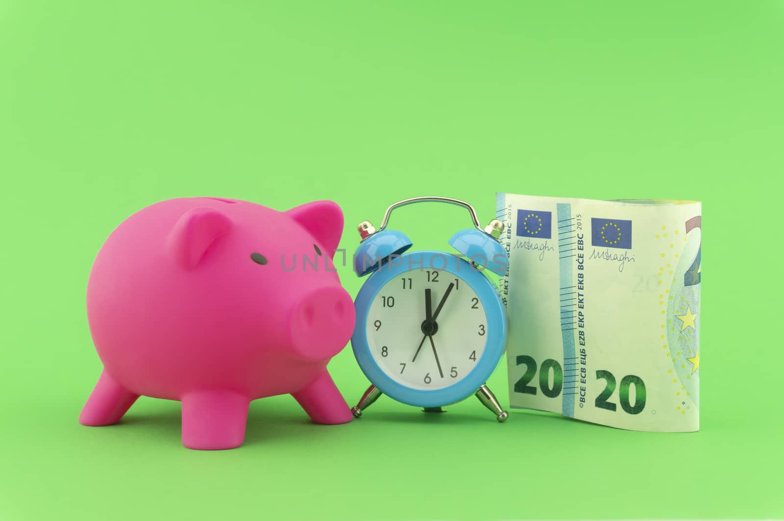 Time management and financial success concept with a 20 Euro bill alongside an alarm clock with piggy bank in the background over green