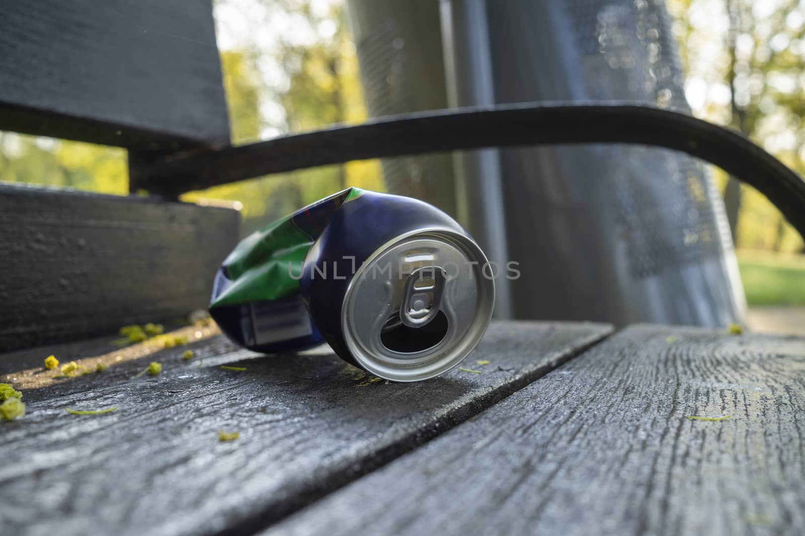 Crumpled can lying on the seat of a rustic wooden a park bench in a low angle close up view