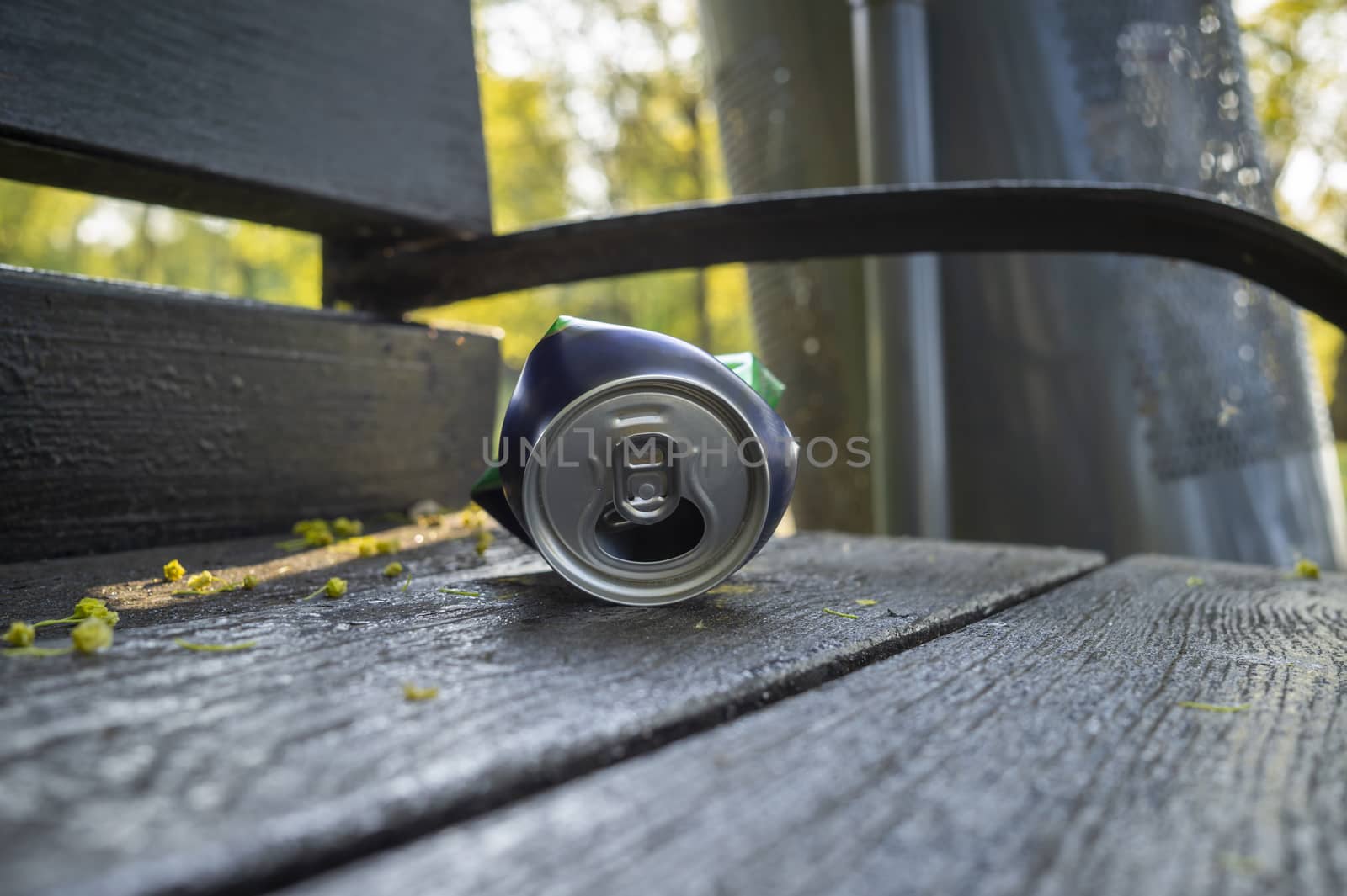 Crumpled can lying on the seat of a rustic wooden a park bench in a low angle close up view