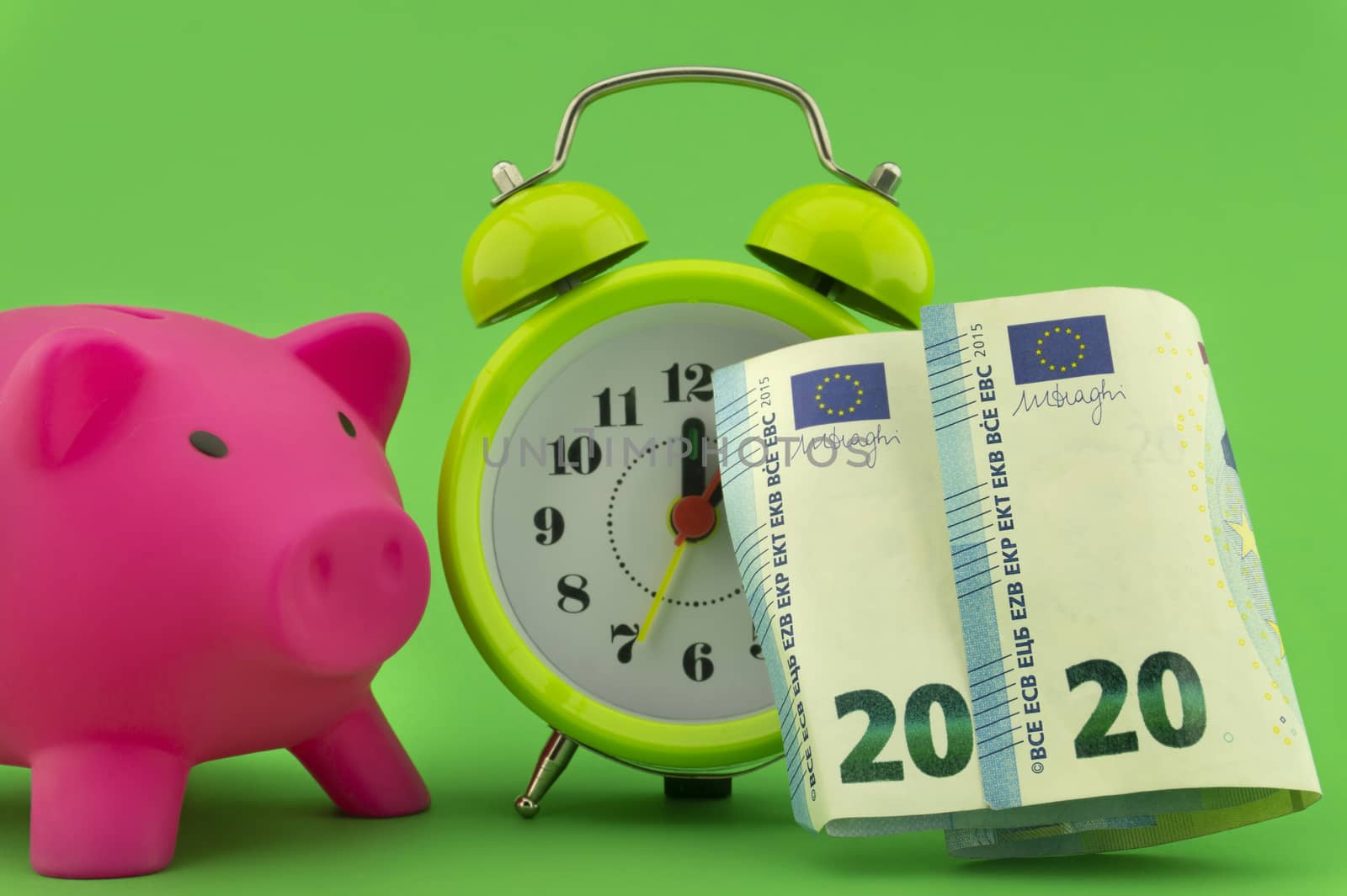 Time management and financial success concept with a 20 Euro bill alongside an alarm clock with piggy bank in the background over green
