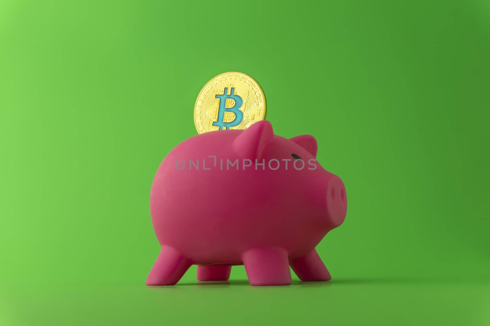 Saving using Bitcoin concept with a virtual gold coin being inserted into a pink piggy bank over a green background